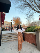 Video of woman outdoors in a chocolate brown high waist faux leather midi skirt & knee high taupe brown boots with tassels. Skirt is faux leather; Straight hem; Midi length side slit pull on design with back zipper for closure.