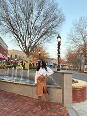 Photo of woman outdoors standing in front of water fountains wearing a chocolate brown high waist faux leather midi skirt with taupe brown knee high boots with tassels. Skirt is faux leather; Straight hem; Midi length side slit pull on design with back zipper for closure.